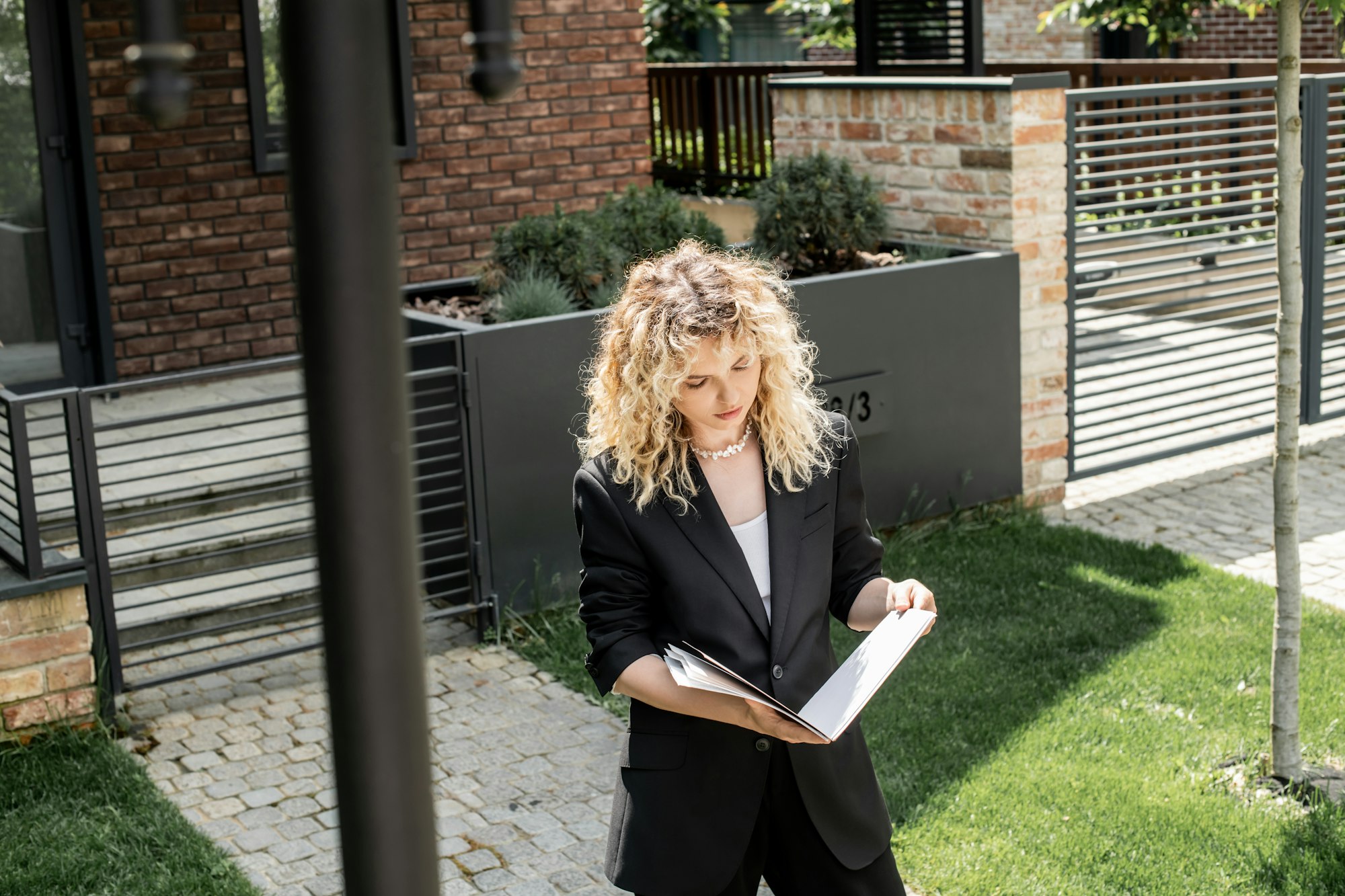 blonde property realtor studying documents in folder next to modern house for sale on city street